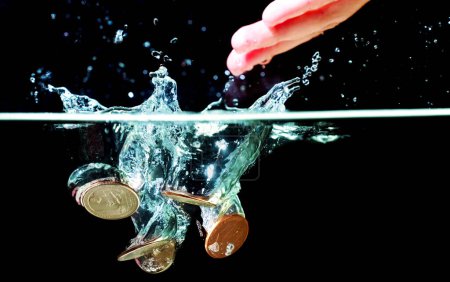Photo for Hand drops some coins underwater with splashes on black. - Royalty Free Image