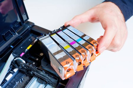 Hand takes one of the fresh ink cartridges placed on a new inkjet printer. Consumables replacement.