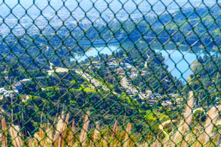 Foto de Hollywood Reservoir, sus pintorescos alrededores, y la extensa ciudad de Los Ángeles capturada desde un mirador en la cima de una colina a través de una cerca de alambre de cadena. - Imagen libre de derechos