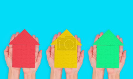 Red, yellow and green jigsaw puzzle houses in hands isolated on blue background. Vibrant education and learning concept.