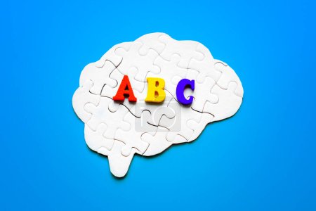 Hirnförmiges Puzzle, geschmückt mit bunten Holzbuchstaben, die das ABC vor einem ruhigen blauen Hintergrund buchstabieren. Konzept Fremdsprachen lernen.