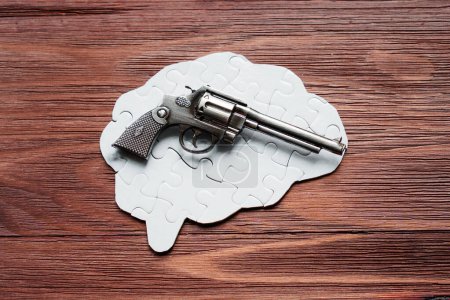 Revolver resting on a human brain-shaped puzzle, against a rustic wooden backdrop. Creativity and destruction concept.