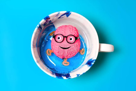 Cerebro sonriente con ojos y gafas pegajosas, flotando casualmente en un anillo inflable dentro de una taza de café, como se ve desde arriba. Concepto de ruptura cerebral.
