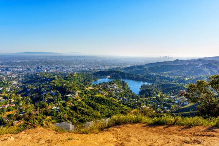 Aerial view of the Hollywood Reservoir and the sprawling city of Los Angeles captured from a hilltop vantage point on a sunny day.