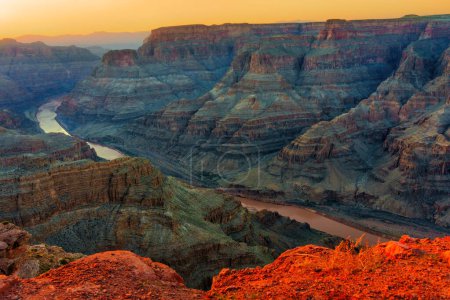 Des formations rocheuses multicouches du majestueux Grand Canyon et une rivière sereine en contrebas vue du haut de la falaise dans la chaleur du soleil couchant.