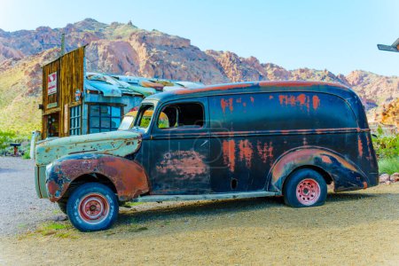Photo for Nelson, Nevada - April 15, 2024: Close-up view of a corroded vintage car with an old body shop and mountains in the background - Royalty Free Image