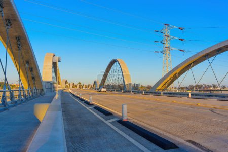 Zeitgenössische Bogenbrücke (6th Street Bridge) mit getrennten Fahrspuren für Fahrzeuge und Fußgänger wird unter einem klaren blauen Himmel eingefangen und präsentiert moderne Technik vor der urbanen Kulisse von LA.
