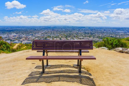 Photo for Twin benches for rest on the Runyon Canyon trail, overlooking Los Angeles under a blue sky dotted with fluffy white clouds. - Royalty Free Image