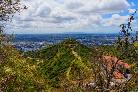 Captivating landscape of Runyon Canyon's green hills, with a clear blue sky filled with thick, white clouds and birds soaring above.