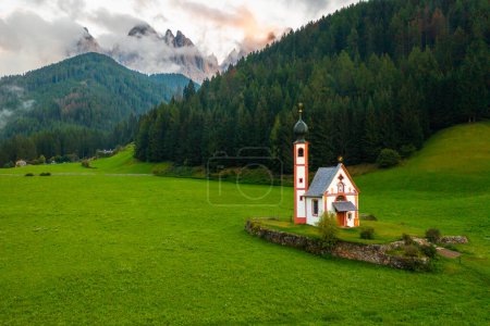 Téléchargez les photos : L'église de St. Johann est dans un bel emplacement pittoresque contre les sommets Geisler couverts de nuages dans le village de Santa Maddalena, Val Di Funes, Italie. - en image libre de droit