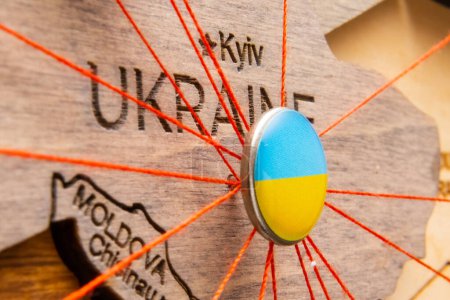 Photo for Ukraine flag on the pushpin with red thread showed the paths of movement or areas of influence in the global economy on the wooden map. Planning of traveling or logistic concept. Network connection. - Royalty Free Image