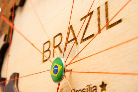 Photo for Brazil flag on the pushpin with red thread showed the paths of movement or areas of influence in the global economy on the wooden map. Planning of traveling or logistic concept. Network connection. - Royalty Free Image