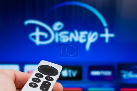 Photo for Disney plus on Apple TV showing on the screen of TV. Man hands switch on television using remote controller, Fabruary 2023, Prague, Czech Republic. - Royalty Free Image