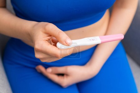 Femme en bleu tenant un test de grossesse positif et tenant le ventre. 