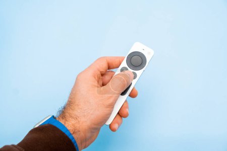 Téléchargez les photos : Apple TV 4k Remote controller in mans hand on the blue background, February 2022, Prague, Czech Republic - en image libre de droit