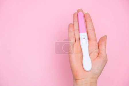 Foto de Mano femenina sosteniendo una prueba de embarazo positiva en el fondo rosa. Planificación del embarazo y el concepto de maternidad con espacio para copias - Imagen libre de derechos