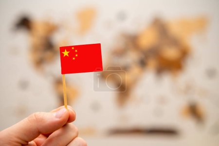Téléchargez les photos : Drapeau de la Chine en mains humaines sur le fond de la carte du monde en bois. Concept d'économie mondiale et de géopolitique. - en image libre de droit