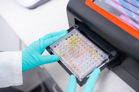 Foto de Un espectrofotómetro de microplacas es utilizado por los científicos para analizar muestras de ADN insertando una microplaca - Imagen libre de derechos