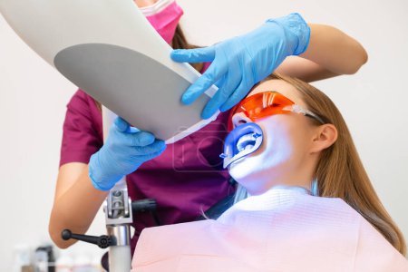 Eine Frau unterzieht sich einer Zahnaufhellung und der Anwendung einer UV-Lampe für den Bleaching-Prozess.