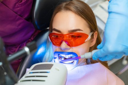 Téléchargez les photos : Aspiration de liquide de la cavité buccale pendant la procédure de blanchiment des dents chez la patiente à la clinique dentaire - en image libre de droit