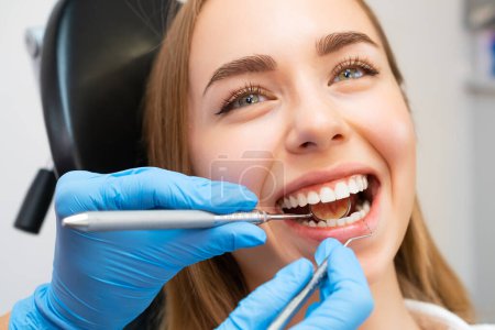 Foto de El dentista, usando guantes, usa un pequeño espejo y una sonda dental para inspeccionar los dientes y encías de los pacientes. - Imagen libre de derechos