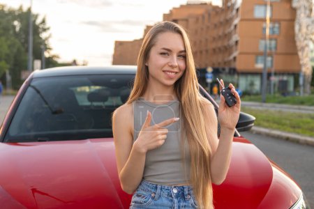 Foto de Mujer joven de pie delante de su nuevo coche y muestra en la llave. - Imagen libre de derechos