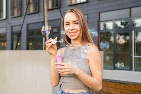 Foto de Una mujer encantada se divierte creando burbujas de jabón y sonriendo cerca de un edificio moderno. - Imagen libre de derechos