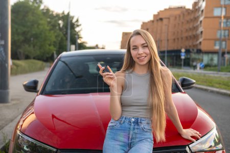 Foto de Una joven conductora sostiene con orgullo la llave del coche delante de su brillante vehículo rojo. - Imagen libre de derechos