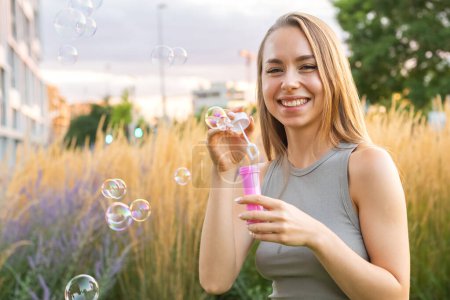 Foto de Una dama alegre con el pelo largo y fluido crea burbujas de jabón y sonrisas en el parque. - Imagen libre de derechos