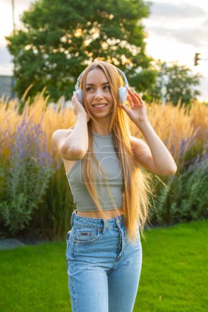 Foto de Retrato de una joven alegre y con estilo escuchar la música con auriculares en el parque, - Imagen libre de derechos