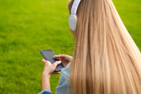 Foto de Mujer joven rubia se sienta con su espalda en los auriculares y escucha música. - Imagen libre de derechos