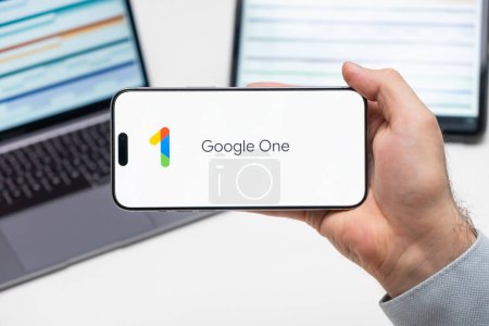 Téléchargez les photos : Google One logo de l'application sur l'écran du téléphone portable détenu par l'homme devant l'ordinateur portable et la tablette, Décembre 2023, Prague, République tchèque - en image libre de droit