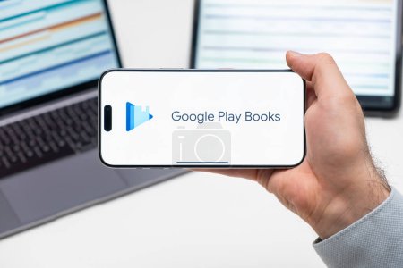 Foto de Google Play Books logotipo de la aplicación en la pantalla del teléfono móvil en poder del hombre delante de la computadora portátil y la tableta, diciembre 2023, Praga, República Checa - Imagen libre de derechos