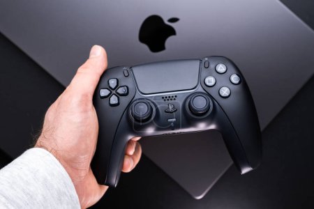 Photo for BERLIN , GERMANY - JANUARY 14 2024: An individual holds a black DualSense controller, perfect for gaming on their Apple MacBook Pro Space Black. - Royalty Free Image