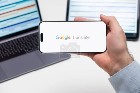 Photo for PRAGUE, CZECH REPUBLIC - JANUARY 21 2024: Google Translate logo on the screen of a cell phone in business mans hand and laptop on the background. - Royalty Free Image