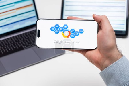 Photo for PRAGUE, CZECH REPUBLIC - JANUARY 21 2024: Google Cloud Platform logo on the screen of a cell phone in business mans hand and laptop on the background. - Royalty Free Image