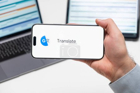 Photo for PRAGUE, CZECH REPUBLIC - JANUARY 21 2024: Google translate logo on the screen of a cell phone in business mans hand and laptop on the background. - Royalty Free Image