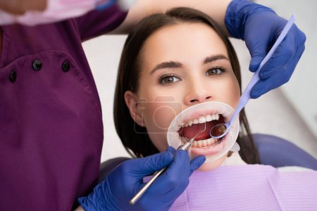 La dentista hembra sopla aire a través de la superficie de secado de los dientes de la saliva para un chequeo adicional. El dentista se prepara para el examen dental de la cavidad oral