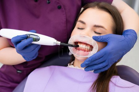 Young brunette woman during teeth whitening procedure with curing UV light.