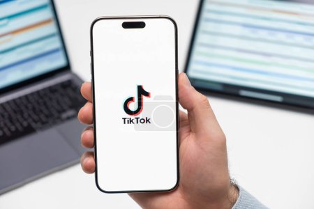 Photo for PRAGUE, CZECH REPUBLIC - JANUARY 21 2024: Tiktok logo on the screen of smartphone in mans hand on the workplace background. - Royalty Free Image