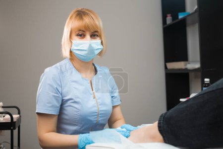 Retrato de podólogo podólogo en máscara facial y uniforme en la clínica. 