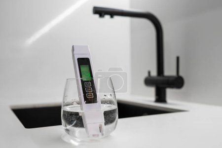 TDS meter immersed into the water in glass shows that the water is clean in modern kitchen. Clean tap water concept. 
