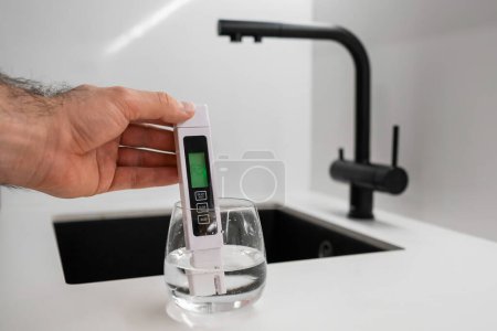 Die Hand taucht TDS-Tester oder Leitfähigkeitsmesser ins Wasser in Glas. zeigt, dass das Wasser sauber ist. 