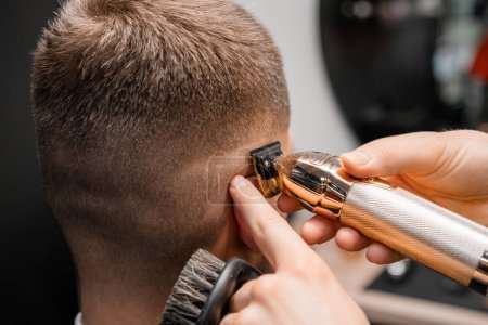 Peluquero afeita el cabello del cliente masculino con un trimmer afilado en primer plano de la barbería. El peluquero experto corta el cabello del hombre en occiput con la máquina en el salón de peluquería