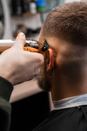 Téléchargez les photos : Master coupe les cheveux du client avec un outil professionnel dans le luxe salon de coiffure gros plan. Barber ne contour de la coiffure droite chez les hommes salon de beauté - en image libre de droit