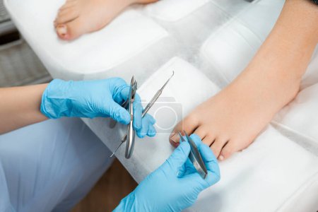 Top view of professional medical pedicure using special nail instruments in the clinic by podologist. 