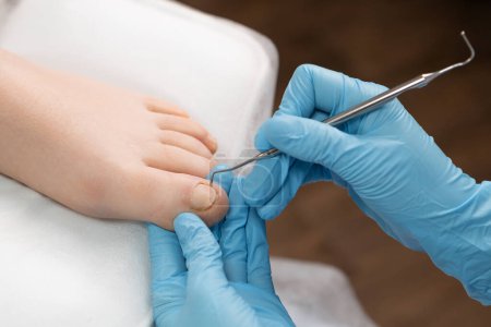 Pedicure master utilise un instrument à ongles pendant le traitement des ongles d'orteil.