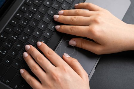 Téléchargez les photos : BERLIN, ALLEMAGNE - 14 AVRIL 2024 : Femme travaillant avec un clavier d'ordinateur portable sur une table noire - en image libre de droit