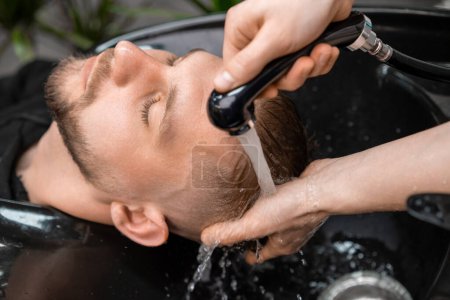 Téléchargez les photos : Skilled hairstylist tenderly rinses a clients hair with warm water in barbershop. - en image libre de droit