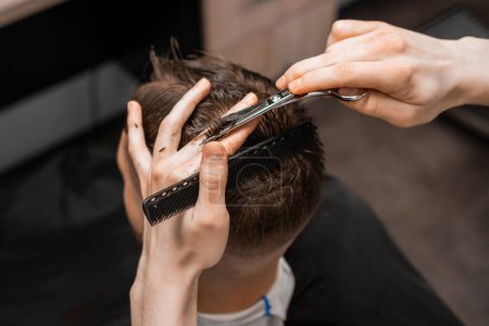 Top view barber uses scissors and comb to style the mans hair at the barbershop